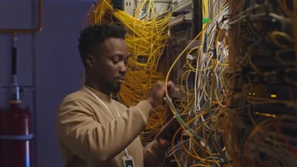 年轻的非裔美国男性信息技术专家在数据中心连接服务器线路时使用数字平板电脑 — 图库视频影像