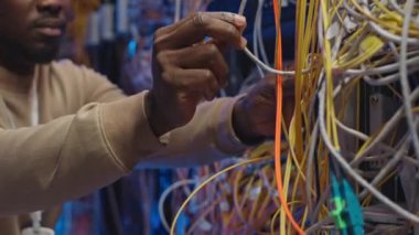 Veri merkezinin işletim rafı sunucu dolabına karmaşık sunucu kablolarını bağlayan Siyah IT mühendisinin kırpılmış görüntüsü