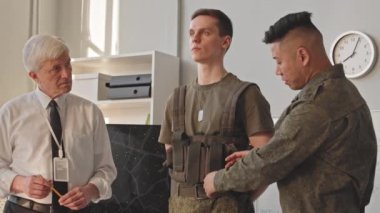 Askeri akademideki seminer sırasında kıdemli profesöre taktik yelek giymeyi öğreten genç bir Asyalı öğrenci.