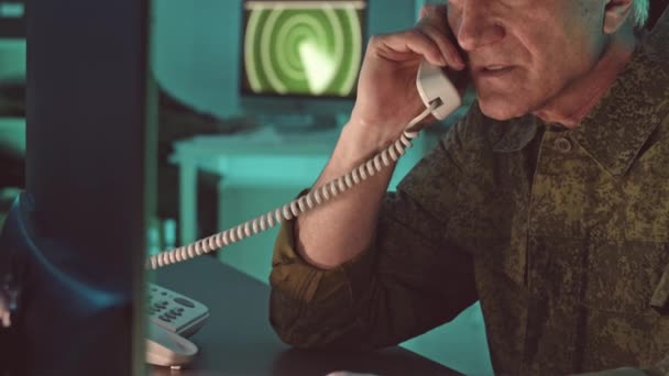 ダークコントロールルームでの操作を監視しながら 電話を作るカモフラージュのユニフォームの成熟した軍事監視司令官のゆっくりとした動き — ストック動画