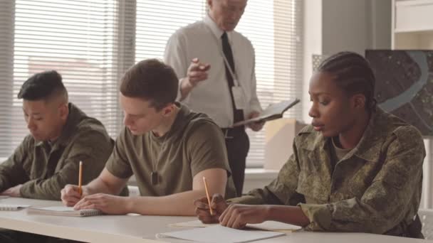 軍事アカデミーの若い多様な男性と女性のキャデットのグループは 教室のセミナーで教授を聞いている間 ノートを作ります — ストック動画