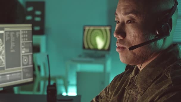 목표를 감시하는 마이크 헤드셋에서 말하는 아시아 장교의 슬로우 클로즈업 어두운 — 비디오
