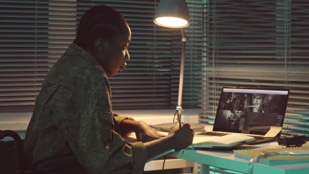 坐在轮椅上监视闭路电视摄像头并在黑暗控制室工作时做笔记的年轻非洲裔美国女军事监视官的慢镜头 — 图库视频影像