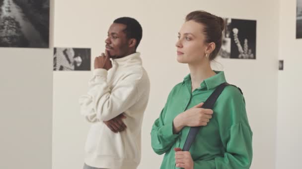 写真ギャラリーで現代美術展に出席しながら壁の抽象的な写真を議論する若い黒人男性と白人女性 — ストック動画