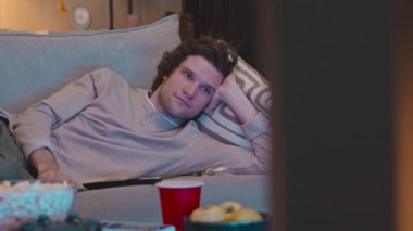 Genç, yakışıklı, beyaz bir adam rahat bir kanepede dinleniyor. Geceleri TV karşısında kanal değiştiriyor.