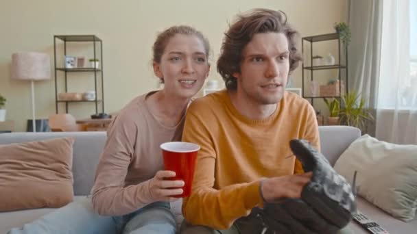年轻快乐的白人夫妇在家里看电视上的棒球 手戴手套的男人 — 图库视频影像