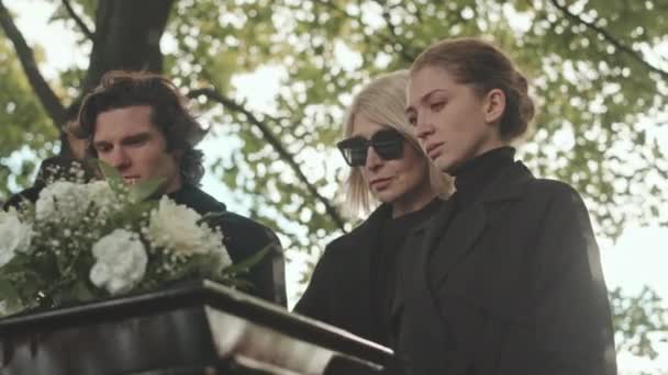 最も親しい友人や家族の喪失を嘆き悲しむ小さなグループは 墓地の棺で立っています — ストック動画