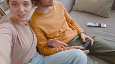 Beyaz bir kadının, erkek arkadaşıyla evde oturup konsolda video oyunu oynarken, oturma odasında kanepede yan yana otururken çekilmiş el kamerasıyla çekilmiş görüntüsü.