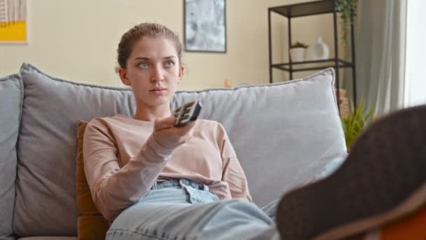若い白人女性は 昼間の切り替えチャンネルでテレビの前でソファーでリラックス — ストック動画