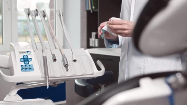 現代の歯科椅子に付いている歯科用具および器械を準備する白い実験室のコートの認識できない歯科医のクロップされたショット — ストック動画