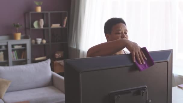 Ältere Afroamerikanerin Wischt Mit Mikrofasertuch Monitor Während Sie Wochenende Hausarbeit — Stockvideo
