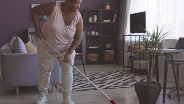 完全な長さのショットプラスサイズのアフリカ系アメリカ人女性は リビングルームで家事をする床をモッピング — ストック動画