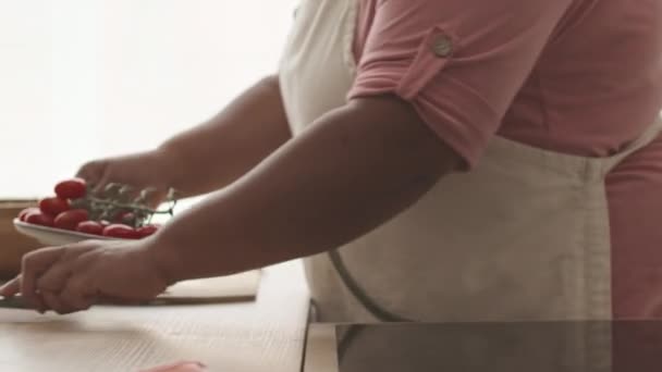 无法辨认的黑人妇女在厨房里做健康午餐的同时切成熟李子形西红柿 — 图库视频影像