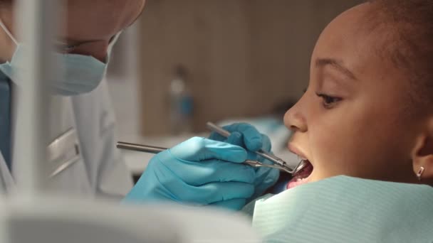 アフリカ系アメリカ人の小さな女の子が歯科クリニックで女性小児歯科医に診察を受ける中間閉鎖 — ストック動画