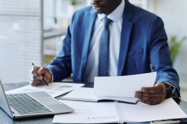 İş yerindeki veri raporlarını analiz eden takım elbiseli, tanınmayan siyahi iş adamlarına yakın çekim.