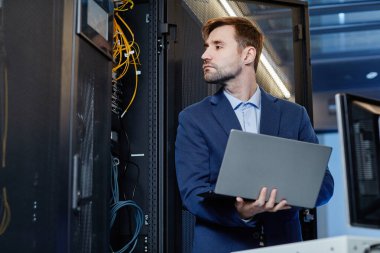 Sunucu odasında internet ağı kurarken elinde dizüstü bilgisayar tutan beyaz bir gencin belden portresi