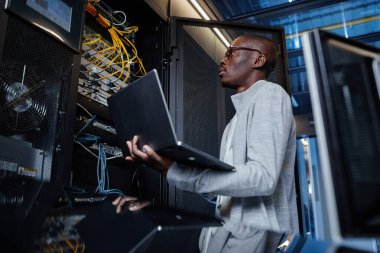 Sunucu odasında internet ağı kurarken bilgisayarını tutan bilişim mühendisi olarak çalışan siyahi adamın yan görünüm portresi
