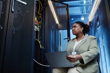 Veri merkezinde sunucu ağı kurarken dizüstü bilgisayar kullanan kadın bilişim mühendisinin düşük açılı görüntüsü, boşluğu kopyala