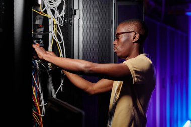 Side view portrait of adult African American man repairing server and setting up data network clipart