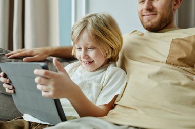 Babasıyla koltukta dinlenirken dijital tablet kullanan gülümseyen çocuğun portresi, boşluğu kopyala