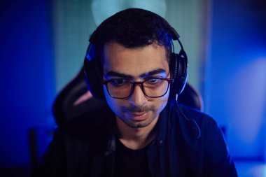 Neon ışıklarda video oyunları oynayan ve oyun kulaklığı takan gözlüklü yetişkin bir adamın ön görünümü.