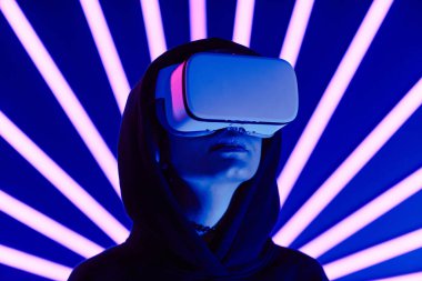 VR kulaklık takan, arka planda neon ışıklı genç bir kadının fotografı. Boşluğu kopyala.