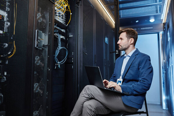 Side view portrait of young system administrator using laptop in server room, copy space