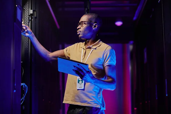 Side view of male system administrator setting up server network in data center lit by neon light