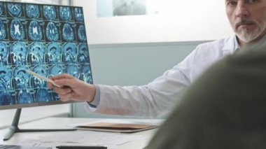 Orta yaşlı beyaz erkek radyoloji uzmanı hasta muayene sırasında MRI beyin taraması gösteriyor.