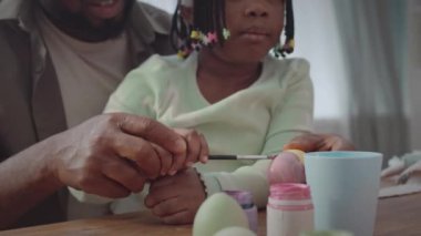 Afrika kökenli Amerikalı bir adam ve küçük kızının sıcak ev ortamında paskalya yumurtalarını boyarken çekilmiş.