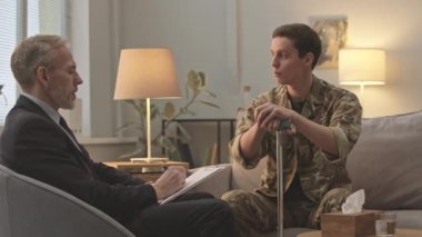 Kamuflaj üniformalı genç beyaz askerin birebir terapi seansı sırasında uzmanla konuşurken orta boy fotoğrafı.