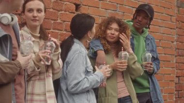 Çok ırklı beş kolej öğrencisinin orta derecede yavaş bir şekilde tuğla duvara yaslanıp sohbet etmesi.