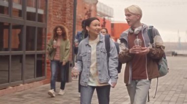 Modern üniversite kampüsünde tuğladan yapılmış bir grup genç birinci sınıf öğrencisi dışarıda yürürken sohbet ediyorlar.