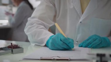 Tanımlanamayan bir bilim adamının beyaz laboratuvar önlüğü ve eldivenleri içinde bilimsel dokümanları incelerken çekilmiş fotoğrafı.