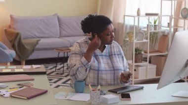 Orta boy Afro-Amerikan kadın kablosuz kulaklık takıyor ve evde serbest çalışırken bilgisayar konferansına başlıyor.