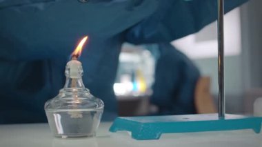 Koruyucu giysiler içinde, cam test tüpünün dibini ısıtan ve laboratuvar ortamında deney yapan tanınmamış bir kimyager.