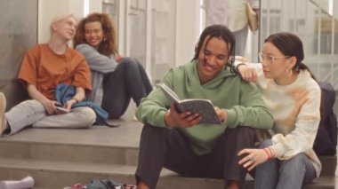 Çok ırklı üniversite öğrencilerinin yavaşlaması koridorda oturmuş ders beklerken sohbet ediyorlar.