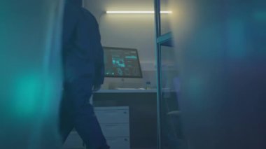 Tanımlanamayan koruyucu giysili biyoteknoloji uzmanının yavaş yavaş test örnekleriyle birlikte gümüş bavul taşıyarak gizli bilimsel laboratuvar boyunca yürümesi.