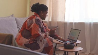 Yan görüş, oturma odasında dizüstü bilgisayarı ve kredi kartıyla internetten alışveriş yapan Afro-Amerikan bir kadının orta boy fotoğrafı.