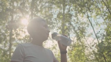 Güneşli bir günde parkta koşarken spor şişesinden su içen yaşlı Asyalı kadının düşük açılı yavaşlığı.