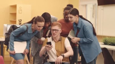 Üniversitedeki çok kültürlü öğrencilerle konuşan Kafkas erkek öğrenci, akıllı telefondan onlara bir şey gösteriyor.
