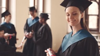 Mezuniyet cüppesi giymiş, diplomalı, beyaz kadın üniversite öğrencisinin yavaş yavaş belini kaldır.