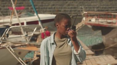 Genç Afrikalı Amerikalı kadın teknisyen telsizle konuşuyor sonra da güneşli bir günde tahta iskelede durup kameraya gülümsüyor.