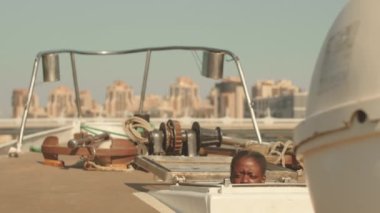 Afrika kökenli Amerikalı genç bir kadının güverteye tırmanışının yavaş yavaş portresi. Kapaktan tırmanıyor, kameraya gülümsüyor, güneşten kıs kıs gülüyor.