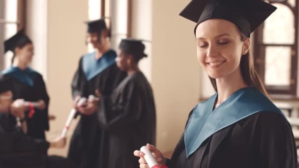 屋内で卒業証書付きのカメラ用ポーズの卒業ガウンで陽気な白人女性ユニークな学生のスローモの肖像画をウエスト — ストック動画