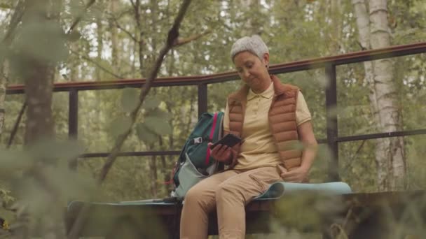 在绿林中独自坐在桥上 用智能手机拍摄的活跃的亚洲老年女性的中景照片 — 图库视频影像