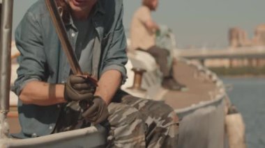 Ahşap güvertede güneş ışığıyla aydınlatılan ve teknenin metal parçalarını özel kumaşla temizleyen denizci görüntüsü.