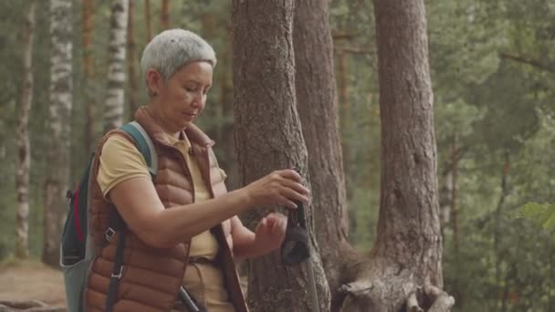 森で休んで自然と新鮮な空気を楽しんでいる間 彼女の手からポールを取るアジアのシニア女性のトレッカーの中型ショット — ストック動画