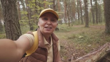 Neşeli, aktif, üst düzey Asyalı bir kadının yaz sonunda ormanda yürüyüş yaparken video blogu kaydettiği el kamerası görüntüleri.