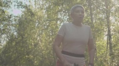 Aktif Asya 'lı yaşlı bir kadının güneşli bir günde parkta tek başına koşarken orta boy fotoğrafı.